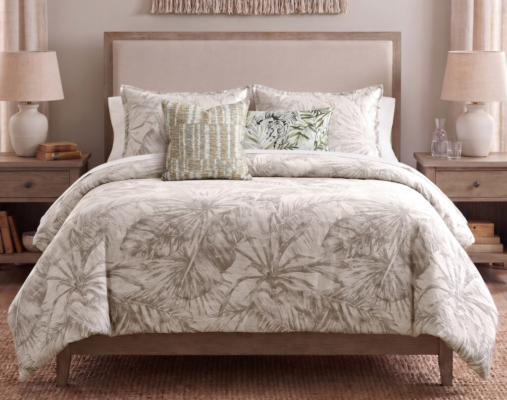 Bed with palm-leaf patterned duvet and decorative pillows on a wooden-framed headboard in a neutral-toned bedroom.