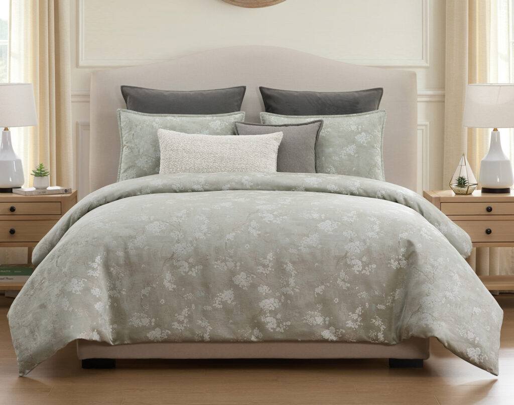 Queen bed with light gray floral bedding and decorative pillows in a bright bedroom setting.