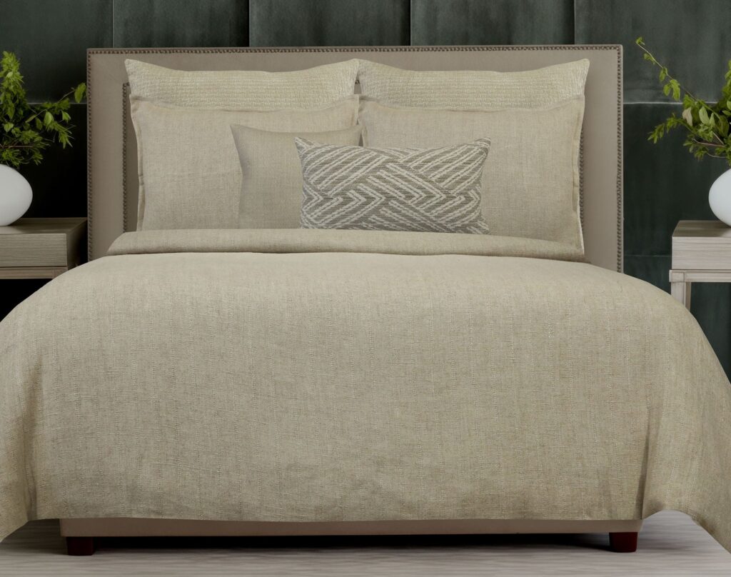 Beige bed with layered pillows and a textured decorative pillow in a neutral-toned bedroom.