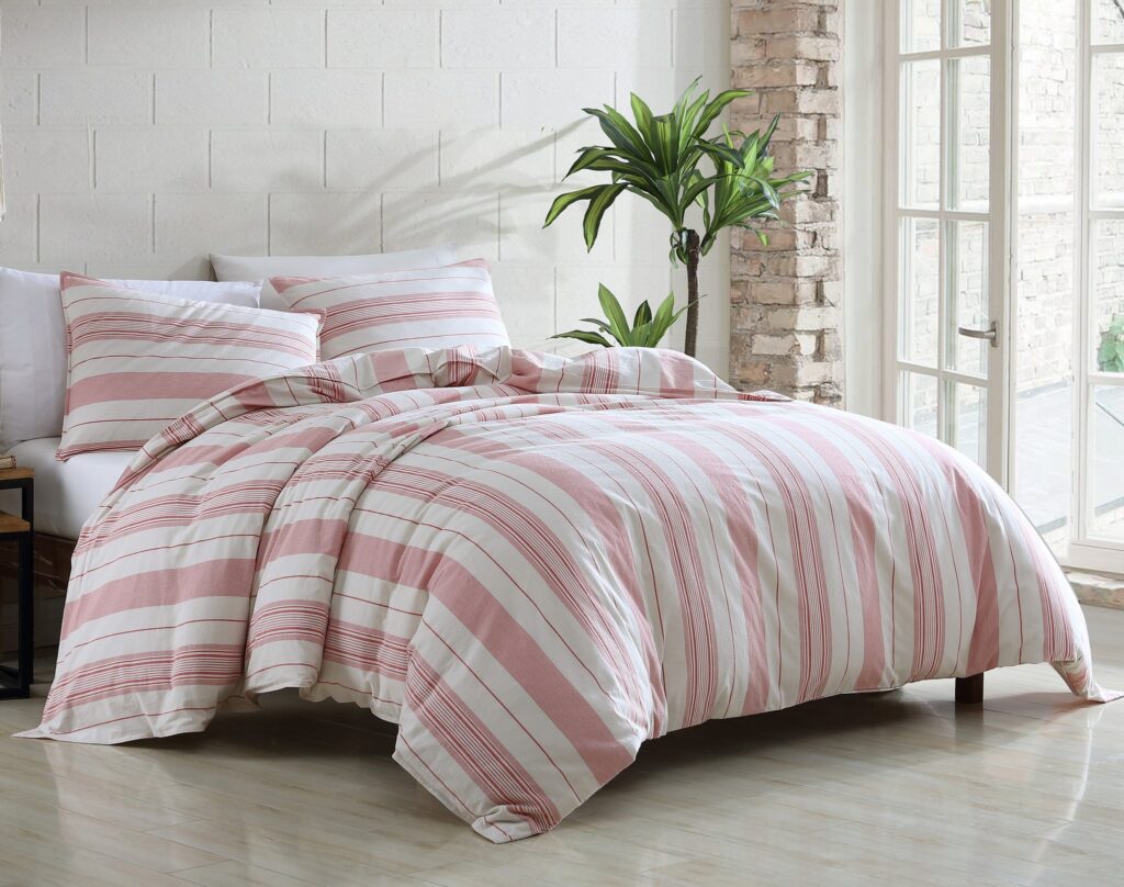 Bedroom scene with a bed dressed in pink and white striped bedding and a green potted plant nearby by a large window.
