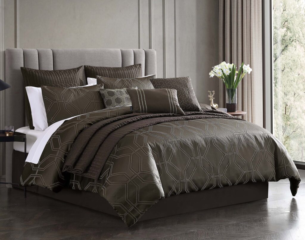 A close-up of a neatly made bed with brown geometric-patterned bedding and multiple matching pillows in a gray upholstered headboard room setting.