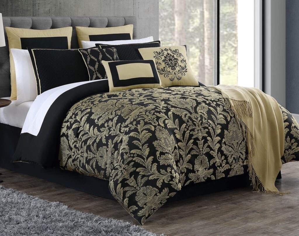 Luxurious bed with black and gold damask bedding, beige and black pillows, and a gray upholstered headboard in a bright bedroom.