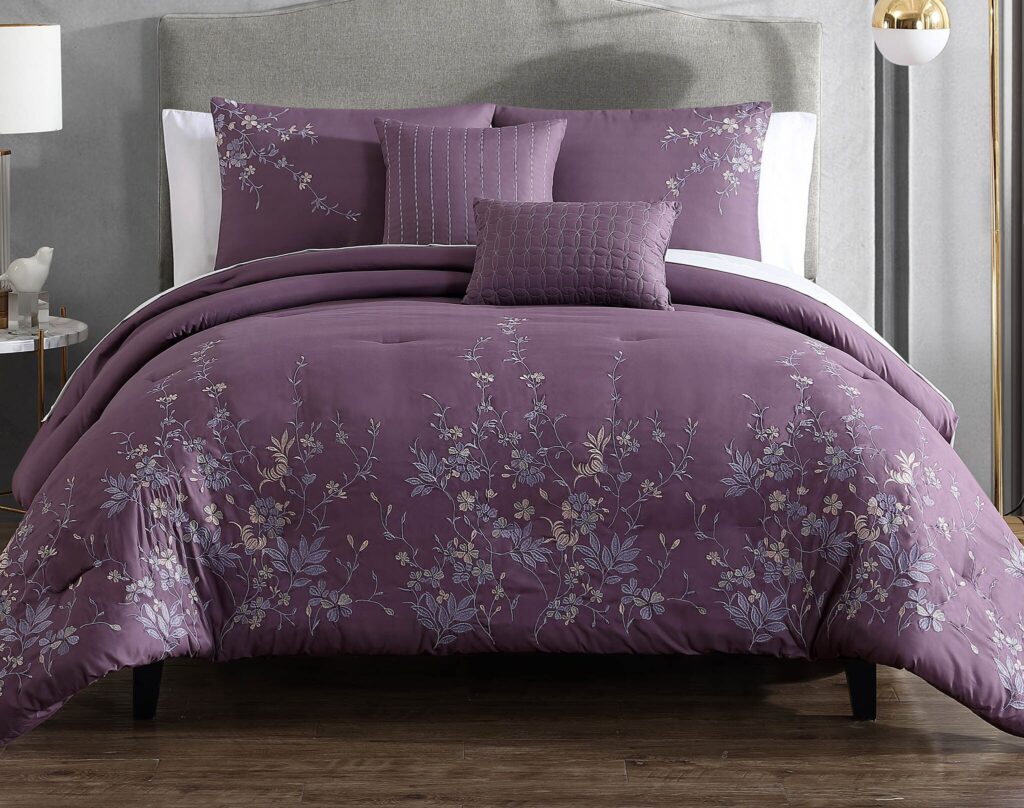 Purple bedding set with delicate silver floral embroidery on a neatly made bed with a gray headboard and white sheets nearby.